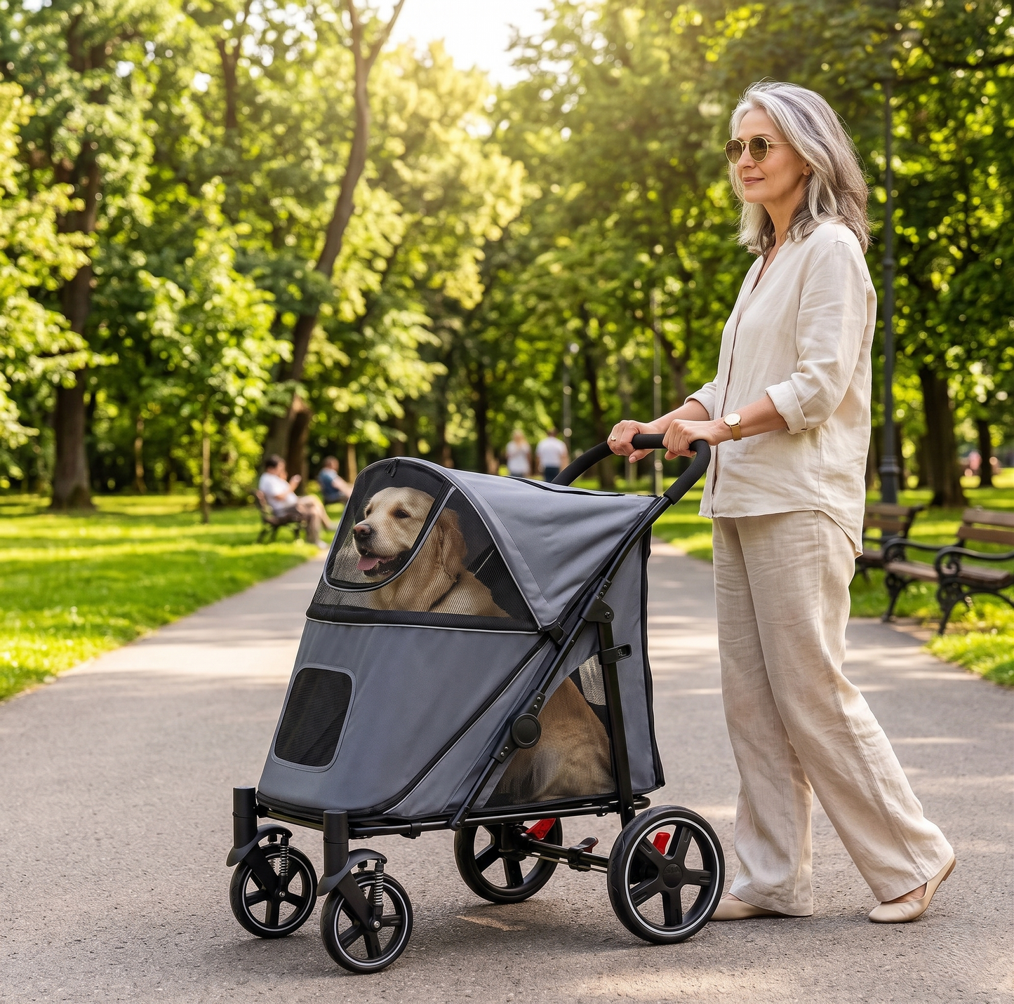 Stylish woman in linen outfit walking a gray large-dog stroller along a sunny park path surrounded by green trees — Golden Retriever sitting comfortably inside, warm afternoon light