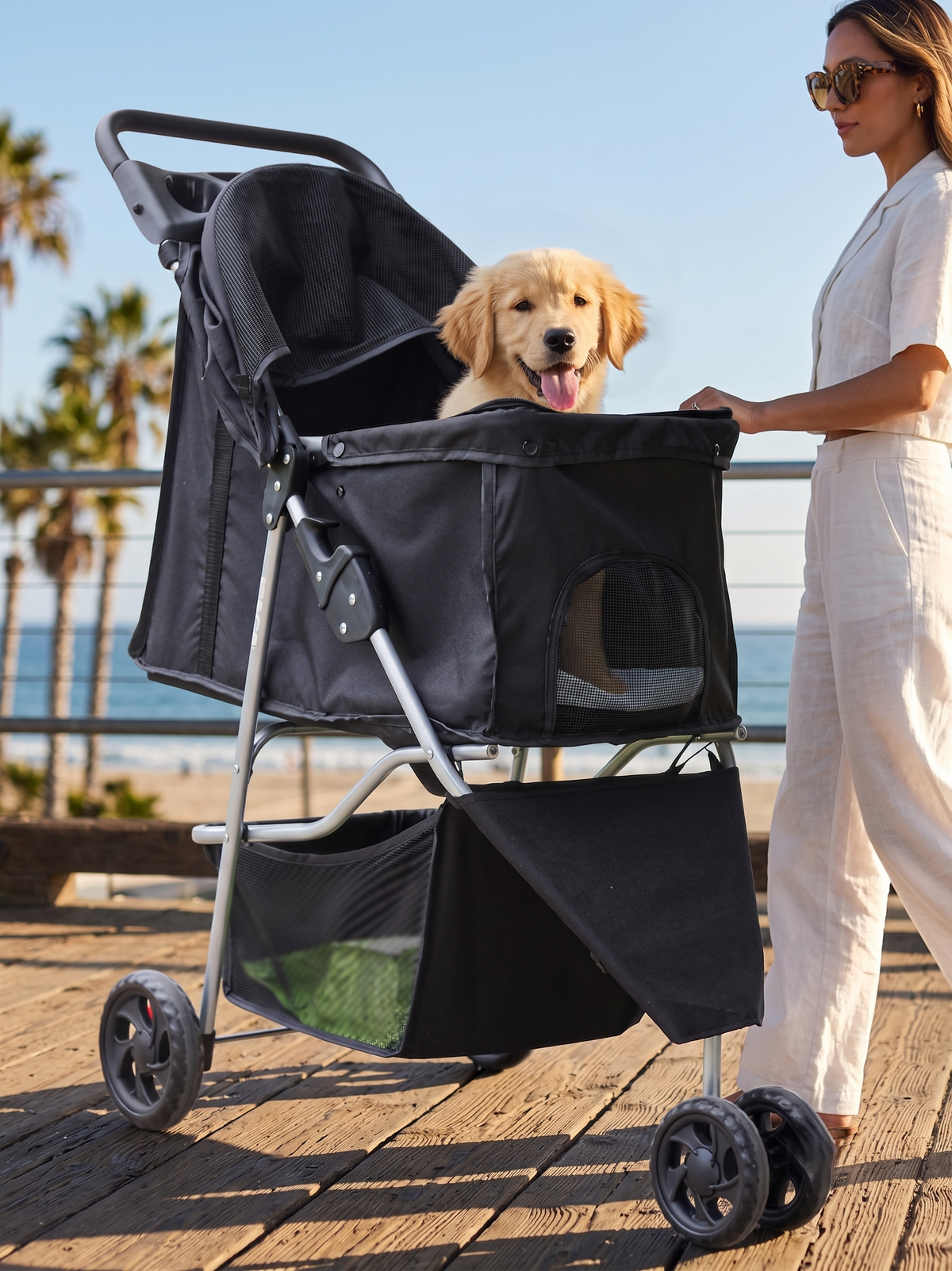 GianfiStore foldable pet stroller on beach boardwalk — golden retriever puppy inside, woman in white outfit, ocean and palm trees background
