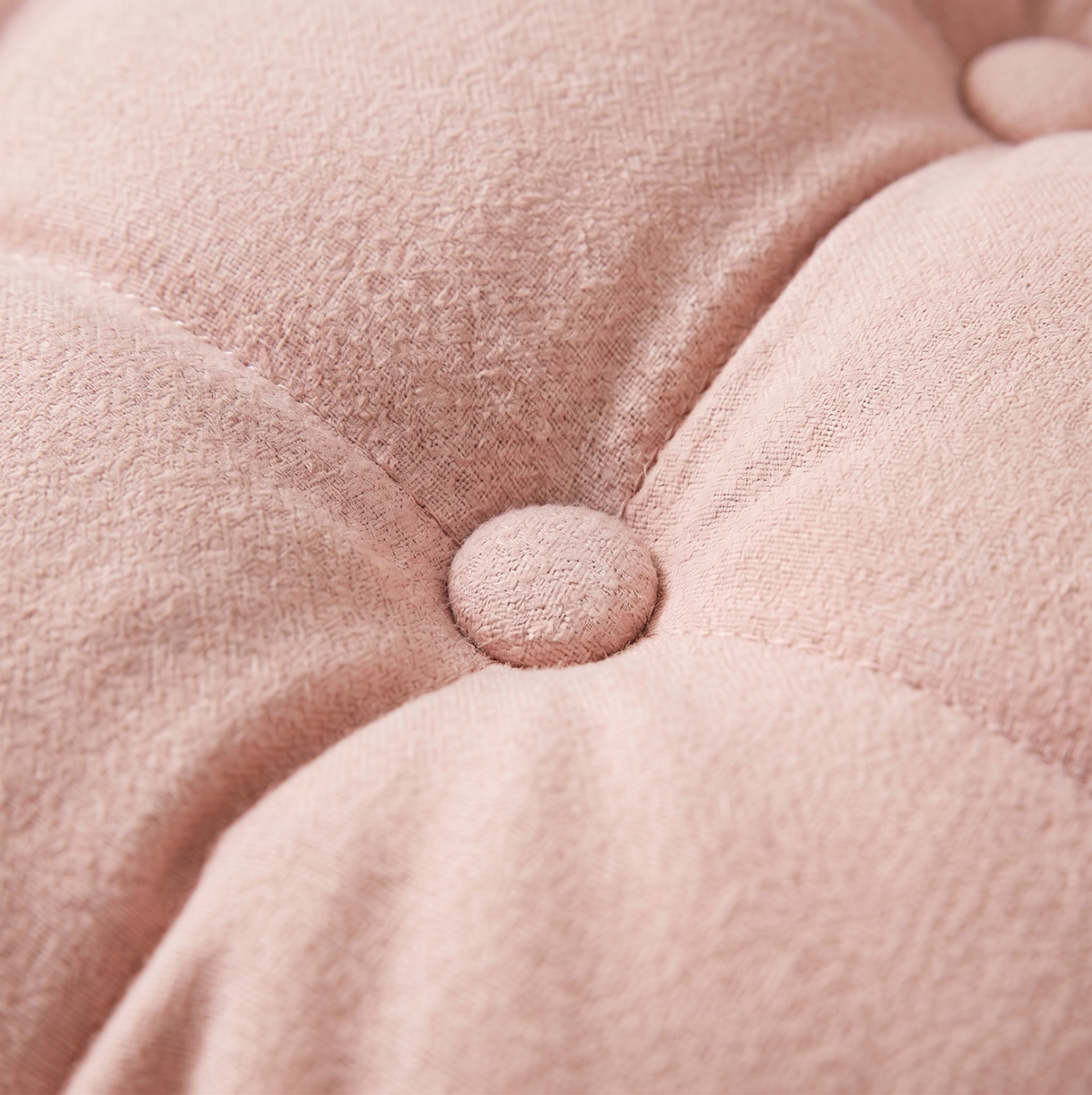 Close-up of the tufted button detail on the plush pink cushion of the water hyacinth cat bed