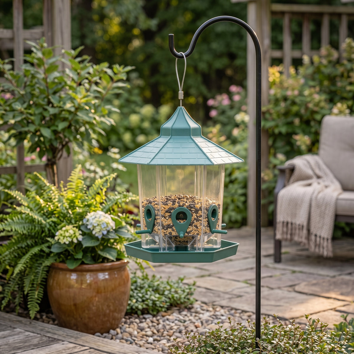 Green hanging bird feeder displayed on a landscaped patio