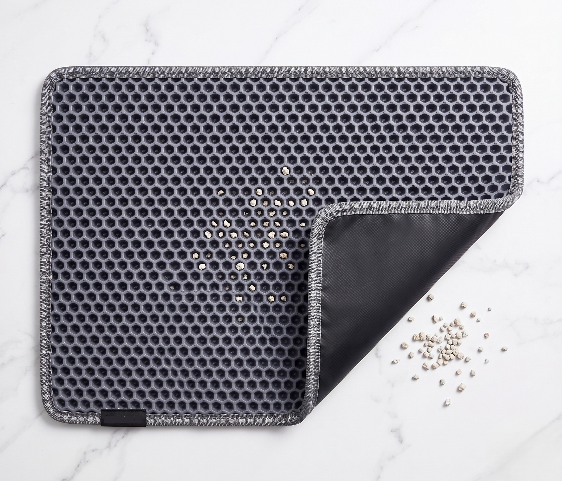 Slate gray double-layer honeycomb cat litter mat partially open showing waterproof black bottom layer, with scattered cat litter granules on white marble surface